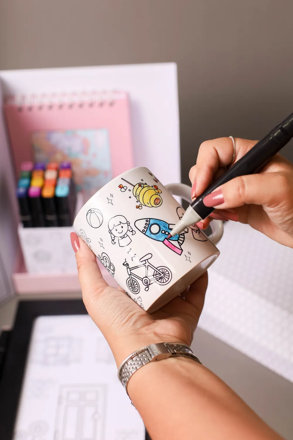 Mãos colorindo a caneca do kit Casinha dos Artistas.